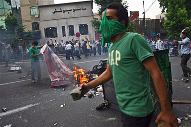 A supporter of Iranian reformist presidential candidate, Mir Hussein Mousavi burns the poster of hard line president Mahmoud Ahmadinejad as others throw stones toward the security forces in Tehran, Saturday, June 13, 2009.