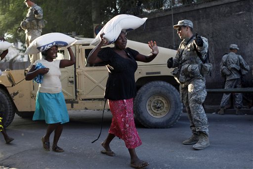 Women carry sacks containing rice during a food distribution watched by U.S. soldiers in Port-au-Prince, Sunday, Jan 31,  2010. Relief workers prepared for a woman-only food distribution system in Haiti's capital, launching a new phase of what they hope will be less cutthroat aid distribution to ensure that families and the weak get supplies following Haiti's devastating Jan. 12 earthquake. (AP  Photo/ Rodrigo Abd) (AP)