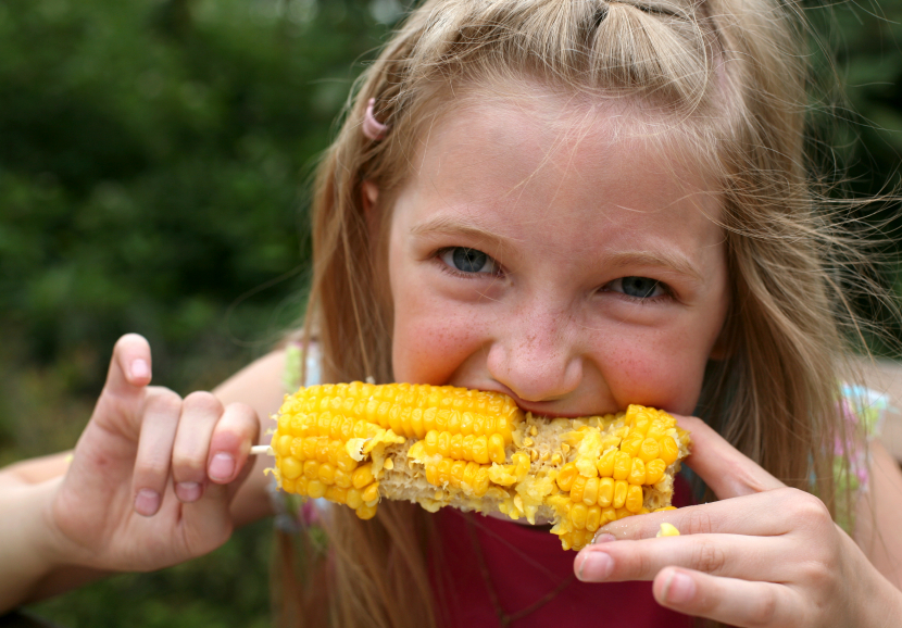 Young funny girl eating a boiled corn