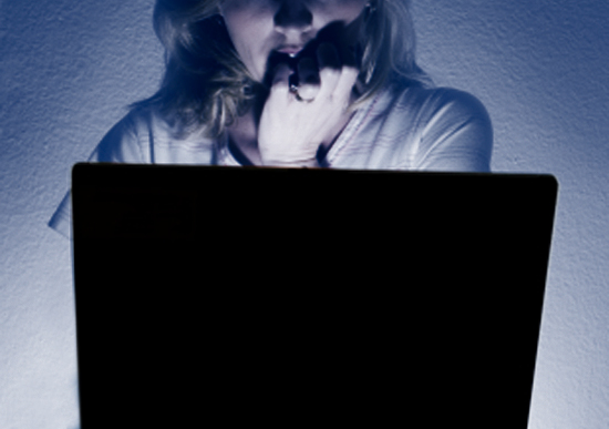 Frightened woman looking at the computer screen in the dark with the light coming from the computer
