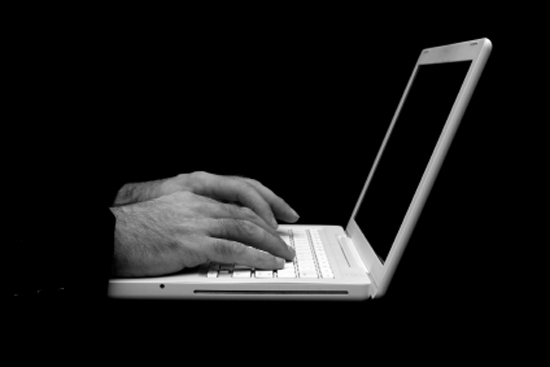 ghostly image of man sitting at desk typing on the keyboard of a white laptop