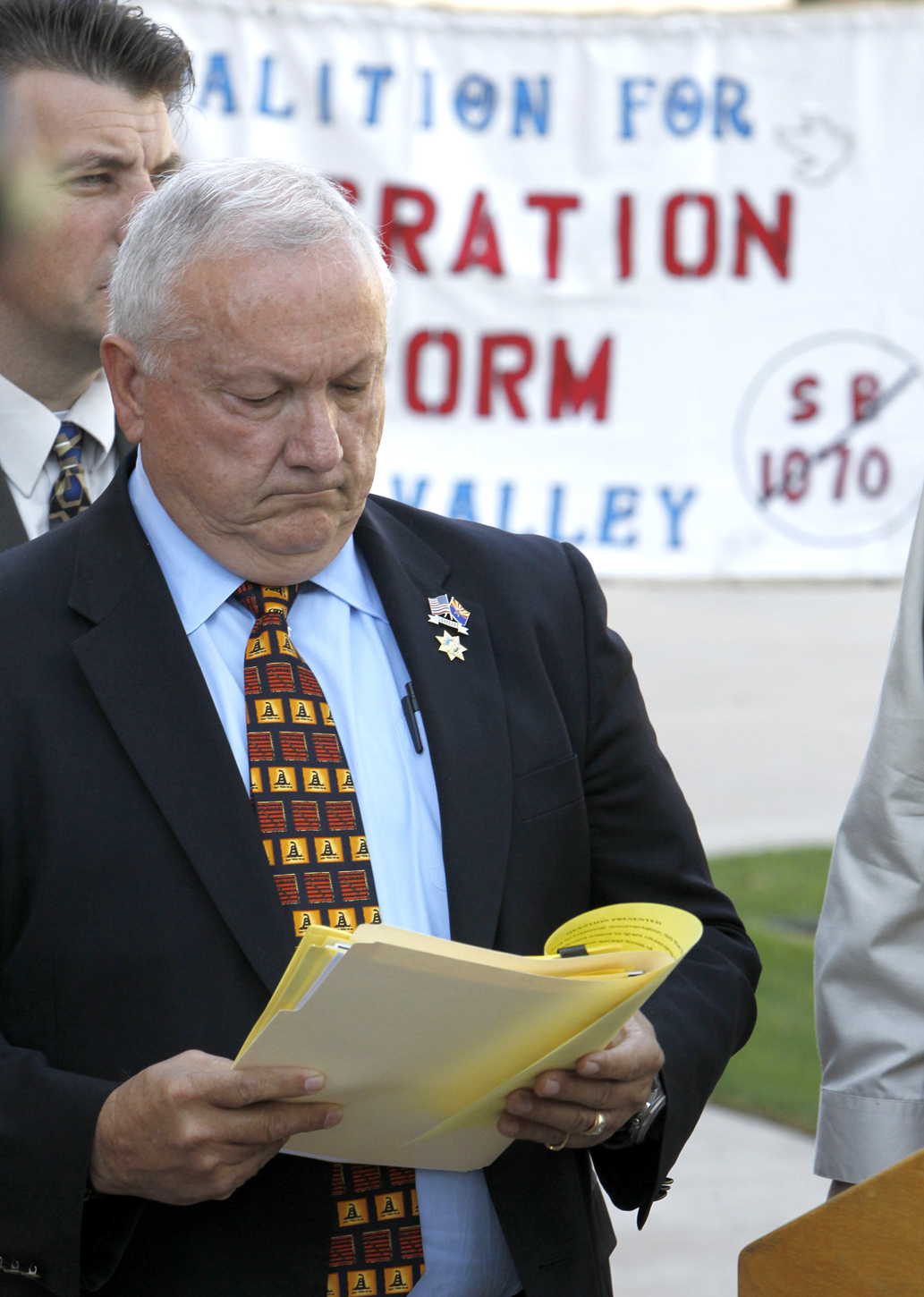 With protesters holding a sign in the background, Arizona state Sen. Russell Pearce, R-Mesa, checks notes before speaking at a news conference about efforts by state legislators to propose legislation to deny U.S. citizenship to children of illegal immigrants Tuesday, Oct. 19, 2010, in Phoenix.  The efforts by the state legislators come amid calls to change the U.S. Constitution's 14th Amendment, which grants automatic citizenship to U.S.-born children of illegal immigrants. (AP Photo/Ross D. Franklin) (Ross D. Franklin)