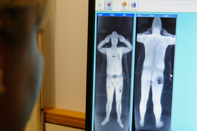 A security officer examines a computer screen showing a scan from a full-body scanner.