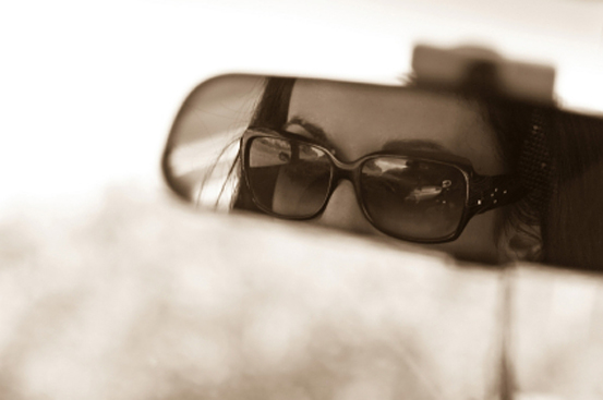 The face of a young woman driving as seen in the rear view mirror. (Unknown)