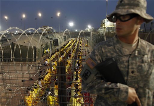 FILE - In this March 16, 2009 file photo, a U.S. soldier stands guard as detainees pray at U.S. military detention facility Camp Bucca, Iraq. A former prison camp that was run by the U.S. military in southern Iraq will be turned into a commercial center with offices, warehouses, aviation and fuel services that will support country's investment activities, an Iraqi official said Monday, Dec. 20, 2010. (AP Photo/Dusan Vranic, File) (AP)