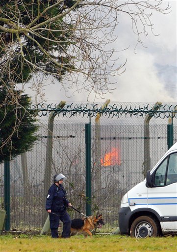 a specialist prison officer dog handler patrols outside the perimeter fence of Ford Prison near Arundel, south England, as the gymnasium building burns in background after about 40 prisoners began a riot and set alight to parts of the open prison, according to the a Ministry of Justice official, Saturday Jan. 1, 2011. (AP Photo / Chris Ison, PA) UNITED KINGDOM OUT - NO SALES - NO ARCHIVES (AP)