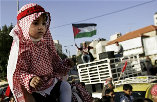 A Palestinian girl sits atop her father's shoulders as a Palestinian flag waves in the background during a march marking the 43rd anniversary of the leftist Popular Front for the Liberation of Palestine (PFLP) in the West Bank city of Ramallah, Saturday, Dec 18, 2010. (AP Photo/Majdi Mohammed) (AP)