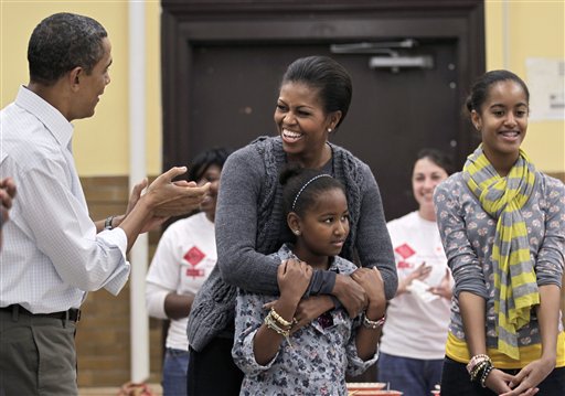 FILE - In this Jan. 17, 2011, file photo first lady Michelle Obama, 47, embracing her daughter Sasha, 9, is surprised by her husband, President Barack Obama, and everyone's singing "Happy Birthday" to her during a community service project at a Washington middle school on the Martin Luther King Jr. holiday. At right is daughter, Malia, 12. Here's Michelle Obama's advice for couples this Valentine's Day: laugh with your partner. She says it's what she and the president do, and it seems to be working. (AP Photo/J. Scott Applewhite) (AP)