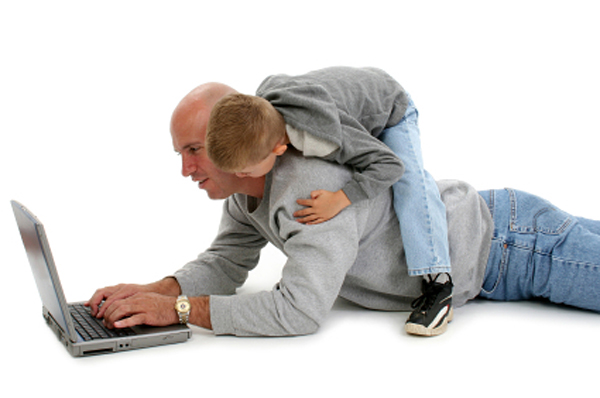 Four year old boy on his father's back while working on laptop. Shot over white. (Jaimie D. Travis)