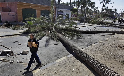A man carrying bread from a bakery walks past felled palm trees used as roadblocks by residents in the Tajoura district of eastern Tripoli, Libya, Saturday, Feb. 26, 2011. Residents there have blocked many streets with roadblocks after protesters demanding Moammar Gadhafi's ouster came under a hail of bullets Friday when pro-regime militiamen opened fire to stop the first significant anti-government marches in days in the Libyan capital.  (AP Photo/Ben Curtis) (AP)
