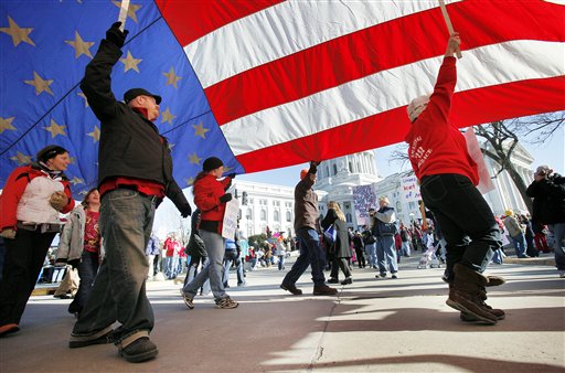 Protesters walk around the state Capitol with an American flag in Madison, Wis., Saturday, Feb. 19, 2011.  A few dozen police officers stood between supporters of Republican Gov. Scott Walker on the muddy east lawn of the Capitol and the much larger group of pro-labor demonstrators who surrounded them.   The protest was peaceful as both sides exchanged chants of Pass the bill! Pass the bill! and Kill the bill! Kill the bill!  The Wisconsin governor, elected in Novembers GOP wave that also gave control of the state Assembly and Senate to Republicans, set off the protests earlier this week by pushing ahead with a measure that would require government workers to contribute more to their health care and pension costs and largely eliminate their collective bargaining rights.    (AP Photo/ Wisconsin State Journal, Michael P. King) (AP)