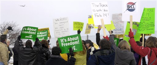 Protesters who identified themselves as Kenosha city and county workers continue to rally as Wisconsin Gov. Scott Walker's plane, upper left, flies away following his news conference about his budget repair bill at the Kenosha Airport in Kenosha, Wis., Friday, Feb. 25, 2011. Walker called on the missing Democratic state senators, including Kenosha's Robert Wirch, to return to the Capitol. (AP Photo/The Journal Times, Mark Hertzberg) (AP)