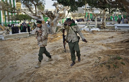 In this photo taken during a government-organised visit for foreign media, a pro-Gadhafi soldier mimics a gun with his hand as he and another walk across freshly-bulldozed ground from which the bodies of opposition dead had been exhumed, according to a resident, in the main square of Zawiya, Libya Friday, March 11, 2011. Libyan Leader Moammar Gadhafi's regime has gained momentum with the capture of Zawiya after days of fierce fighting with rebels, in a key test of the government's ability to maintain its hold on the Libyan capital and surrounding areas. (AP Photo/Ben Curtis) (AP)