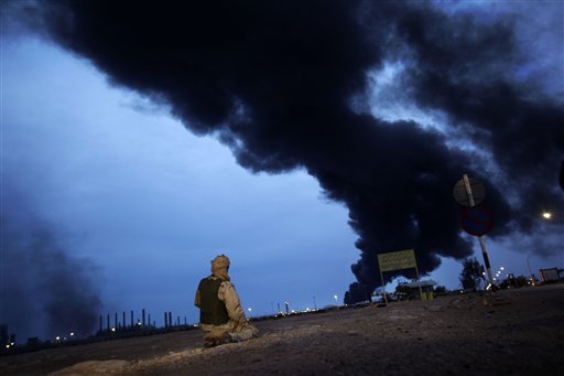 In this photo taken during a government-organised visit for foreign media, a pro-Gadhafi fighter makes his evening prayers in the desert as a plume of smoke rises from the burning oil refinery in Ras Lanouf, 380 miles (615 kilometers) southeast of the capital Tripoli, in Libya Saturday, March 12, 2011. (AP Photo/Ben Curtis) (AP)