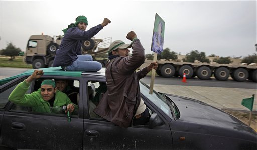 Pro-Gadhafi supporters in a car speed past a vehicle used to transport tanks from the Libyan military's elite Khamis Brigade, led by Gadhafi's youngest son Khamis Gadhafi, hours after the Khamis units were deployed on the road in Harshan, 10km east of Zawiya, in Libya, Monday, Feb. 28, 2011. Rebel forces in Zawiya were locked in a standoff with Gadhafi loyalists and residents inside the city said they were anticipating a possible attack. (AP Photo/Ben Curtis) (AP)