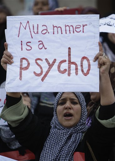 A Libyan protester holds up a sign as she shouts slogans against Libyan leader Moammar Ghadafi during the demonstration before Friday prayers, in Benghazi, Libya, on Friday Feb. 25, 2011. Militias loyal to Moammar Gadhafi opened fire on protesters streaming out of mosques in the Libyan capital on Friday, demanding the regime's ouster, witnesses said, reporting at least four killed. Across rebellious cities in the east, tens of thousands held rallies in support of the first Tripoli protests in days. (AP Photo/Hussein Malla) (AP)