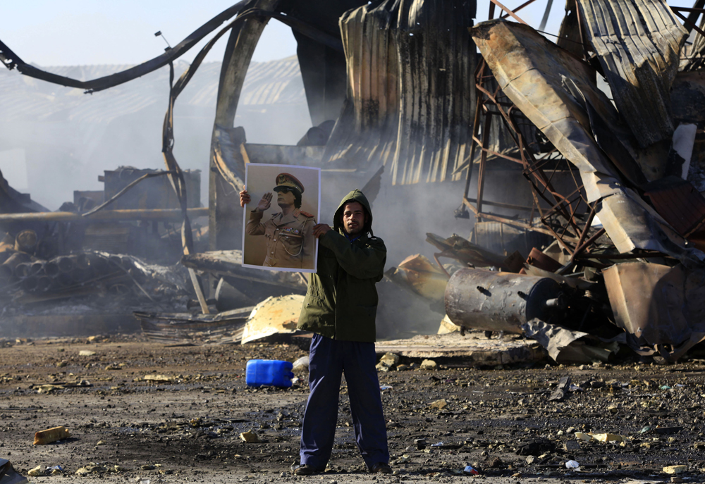 EDITOR'S NOTE: PICTURE TAKEN ON GUIDED GOVERNMENT TOUR

A Libyan holds a poster of Libya's leader Muammar Gaddafi at a naval military facility damaged by coalition forces air strikes last night in People's Port in eastern Tripoli March 22, 2011. Anti-aircraft fire and explosions reverberated across Tripoli for a third night on Monday and state television said several sites had come under attack in the capital. REUTERS/Ahmed Jadallah (LIBYA - Tags: CIVIL UNREST CONFLICT POLITICS) (Â© Ahmed Jadallah / Reuters)