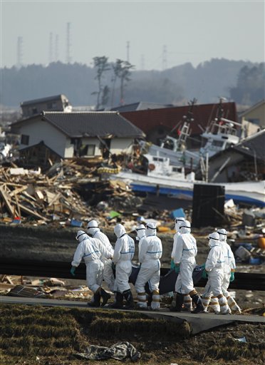 Japanese police officers carry a body during a search and recovery operation for missing victims in the area devastated by the March 11 earthquake and tsunami in Namie, Fukushima Prefecture, northeastern Japan, Friday, April 15, 2011. In the background is part of the Fukushima Dai-ichi nuclear complex.(AP Photo/Hiro Komae) (AP)
