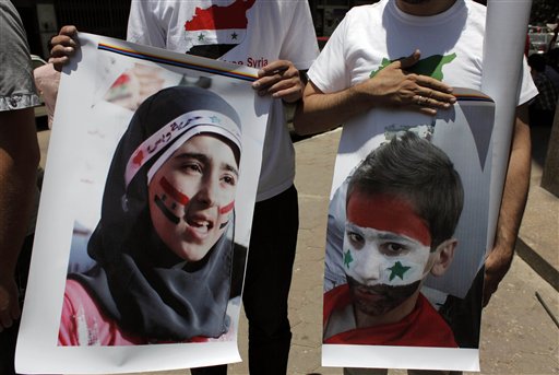 Two protesters carry posters with pictures of unidentified relatives in Syria,  with the Syrian flag colors painted on their faces during an anti-Syrian regime rally near the Syrian embassy in Cairo, Egypt Tuesday, July 5, 2011. Syrian troops fired Tuesday on residents who set up makeshift roadblocks to prevent the advance of tanks ringing the city of Hama, which has become a flashpoint of the uprising against autocratic President Bashar Assad, activists said. (AP Photo/Nasser Nasser) (AP)