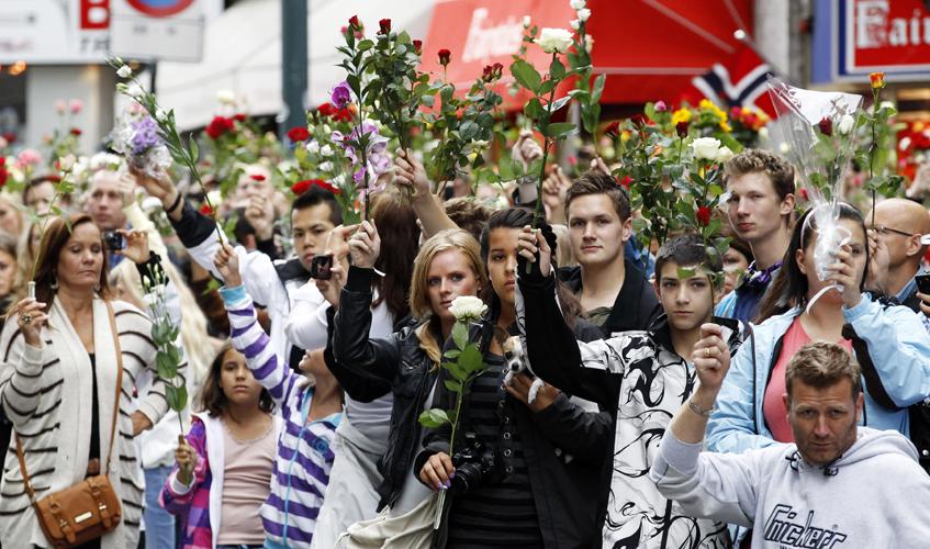 People hold up flowers as they take part in a memorial march for the victims of the killing spree and bomb blast in downtown Oslo