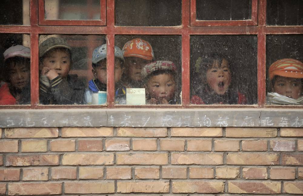 Children look out from a window of their classroom at a rural primary school in Min county, Gansu province June 1, 2011