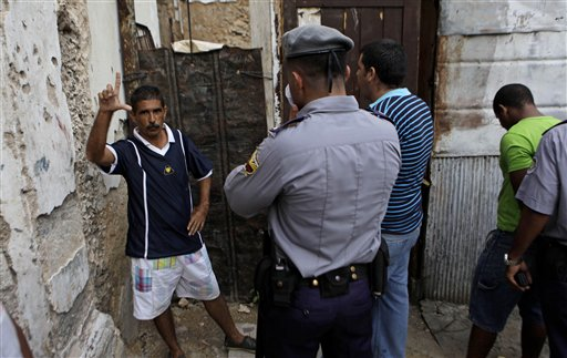A dissident signs the letter "L" for the Spanish word "libertad" or freedom as he is detained by police during a procession celebrating Cuba's patron saint in Havana, Cuba, Thursday Sept. 8, 2011