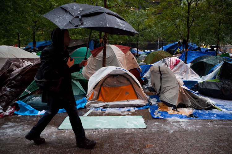 A pedestrian walks by snow covered Occupy Wall Street tents during a snowstorm in Zuccotti Park, New York. (AP)