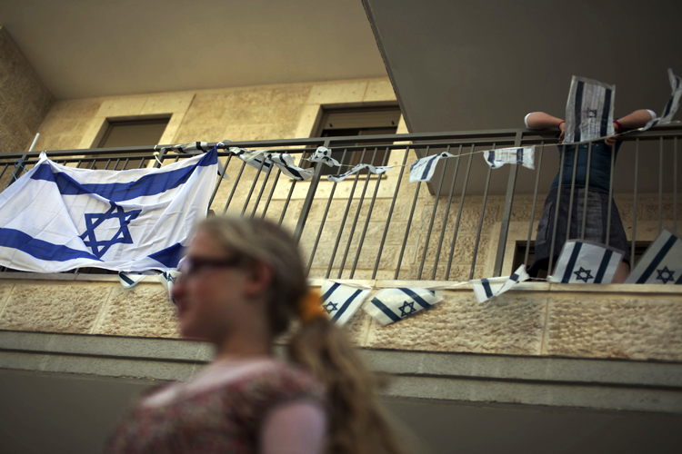 A woman walks past an Israeli flags hanging on a balcony before a ribbon-cutting ceremony at a recently built Jewish settlement in the East Jerusalem neighbourhood of Ras al-Amud May 25, 2011. (Reuters)