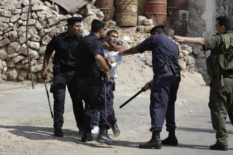An Israeli soldier gestures as Palestinian policemen detain a youth during clashes in the West Bank city of Hebron September 21, 2011. (Ammar Awad / Reuters)