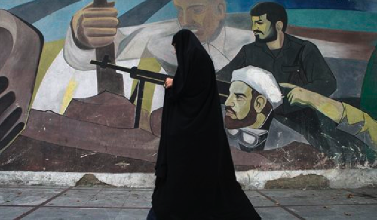 In this Tuesday, Oct. 18, 2011 photo, an Iranian woman walks past a mural depicting members of Basij paramilitary force, portraying Iranians' solidarity against their enemies, in Tehran, Iran. (AP Photo/Vahid Salemi)