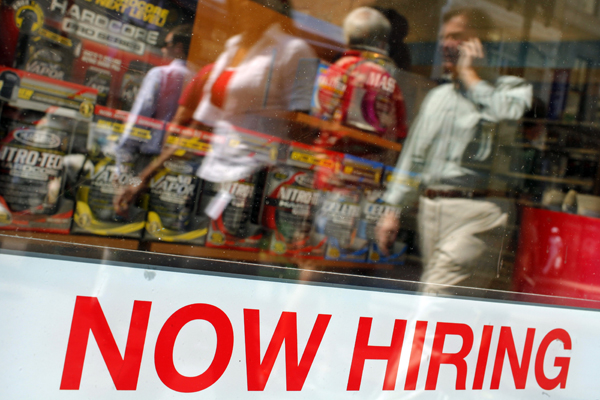 Pedestrians walk past a "Now Hiring" sign in the window of a GNC shop (Brian Snyder / Reuters)