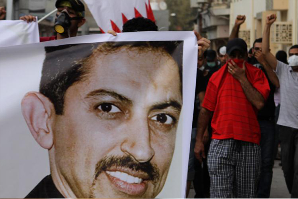 Bahraini anti-government protesters, protecting their faces from tear gas, carry national flags and a picture of jailed human rights activist Abdulhadi al-Khawaja at a protest on ApPril 4. (AP/Hasan Jamali)