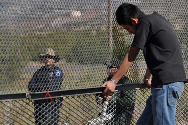 A man in Ciudad Juarez, Mexico, stands next to the border fence as two U.S. law enforcement officers look on from the U.S. side of the fence. (AP/Raymundo Ruiz)