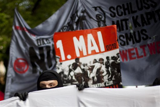 A masked left-wing protester holds a poster as he walks with other demonstrators at a rally to mark May Day in Berlin's district Kreuzberg, Tuesday, May 1, 2012. (AP Photo/Markus Schreiber)