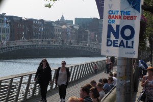 Dubliners bask in the sunshine on the River Liffey on Friday, May 25, 2012, as an anti-EU poster advises voters to reject the European Union's fiscal treaty in Dublin, Ireland. (AP Photo/Shawn Pogatchnik)
