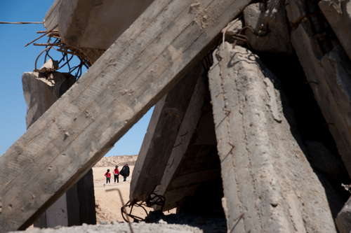Palestinians in Gaza walk by damage from an Israeli shelling (Shutterstock)