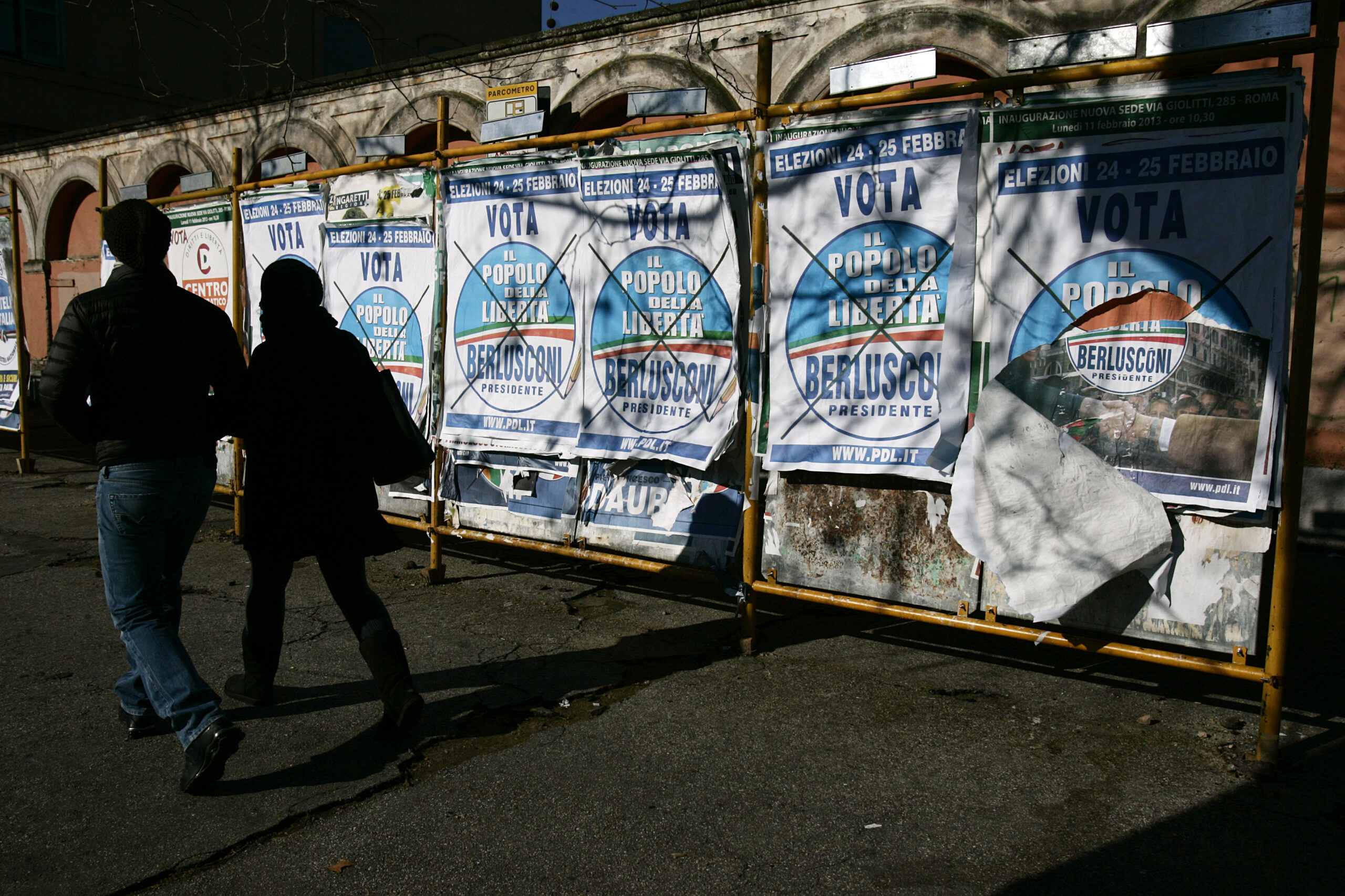A couple walks past electoral posters of People of Freedom party reading: "February 24-25 Vote People of Freedom, Berlusconi for President", in Rome. (AP/Gregorio Borgia)