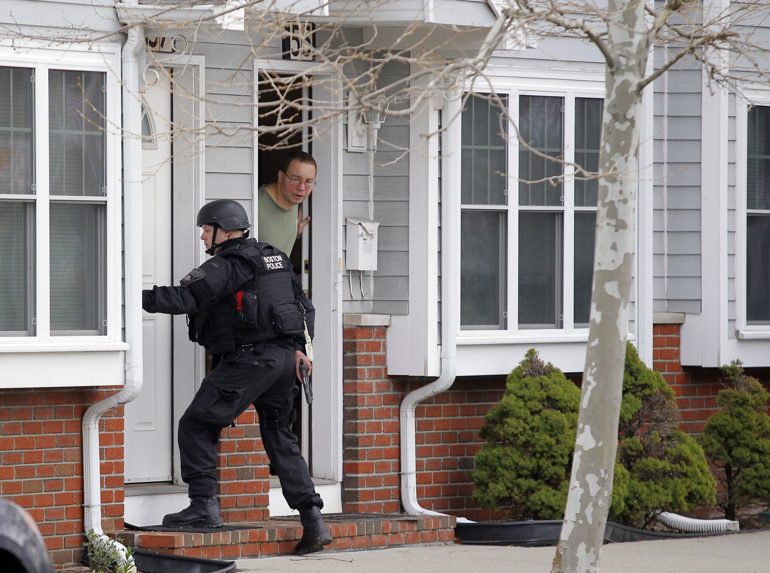 A man looks out his door as a SWAT team member knocks on his neighbor's door as they search for the remaining suspect in the Boston Marathon bombings in Watertown, Mass., April 19, 2013. (Reuters)
