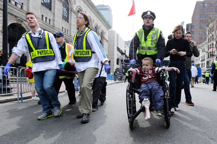 A Boston police officer wheels in injured boy down Boylston Street as medical workers carry an injured runner following an explosion during the 2013 Boston Marathon. (AP/Charles Krupa)