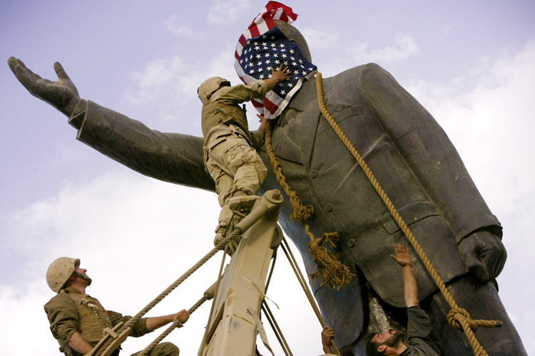 Cpl. Edward Chin, of the 3rd Battalion, 4th Marines Regiment, covers the face of a statue of Saddam Hussein with an American flag before toppling the statue in downtown in Bagdhad Wednesday, April 9, 2003. Moments later the American flag was removed. (AP/Jerome Delay)