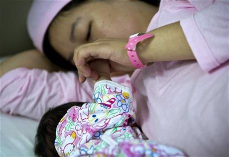 In this Wednesday, Aug. 7, 2013 photo, Chinese new mother Qi Wenjuan holds her 1-day-old son's hand while breastfeeding him at Tiantan Hospital’s maternity ward in Beijing, China. China’s rates of breastfeeding are among the world’s lowest. But health workers and the government are trying to revive the tradition, and a drumbeat of safety scares over commercially produced milk is giving them new leverage. (AP Photo/Andy Wong)
