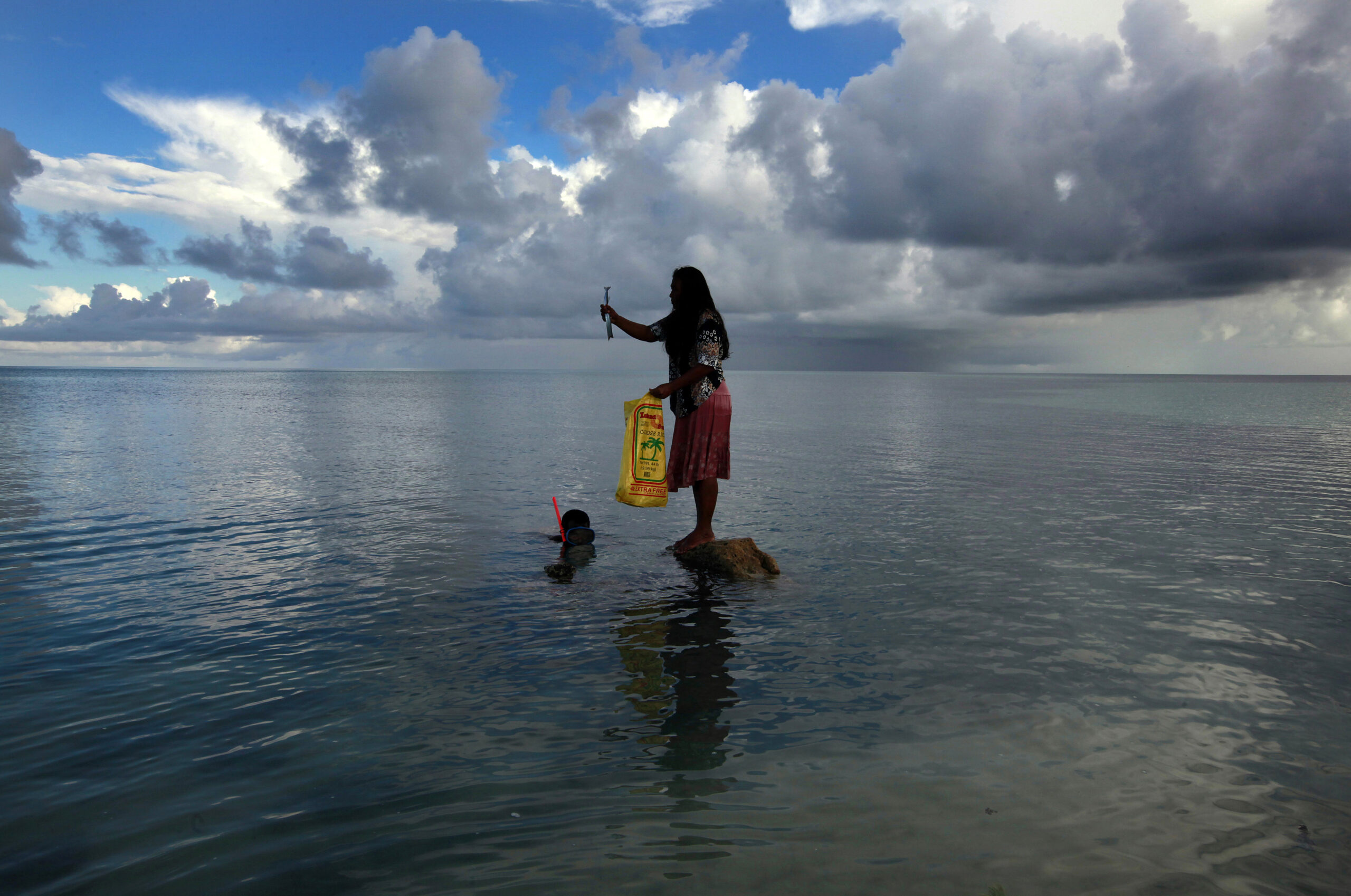 Binata Pinata stands on top of a rock holding a fish her husband Kaibakia just caught off Bikeman islet, located off South Tarawa in the central Pacific island nation of Kiribati, May 25, 2013. (Reuters)