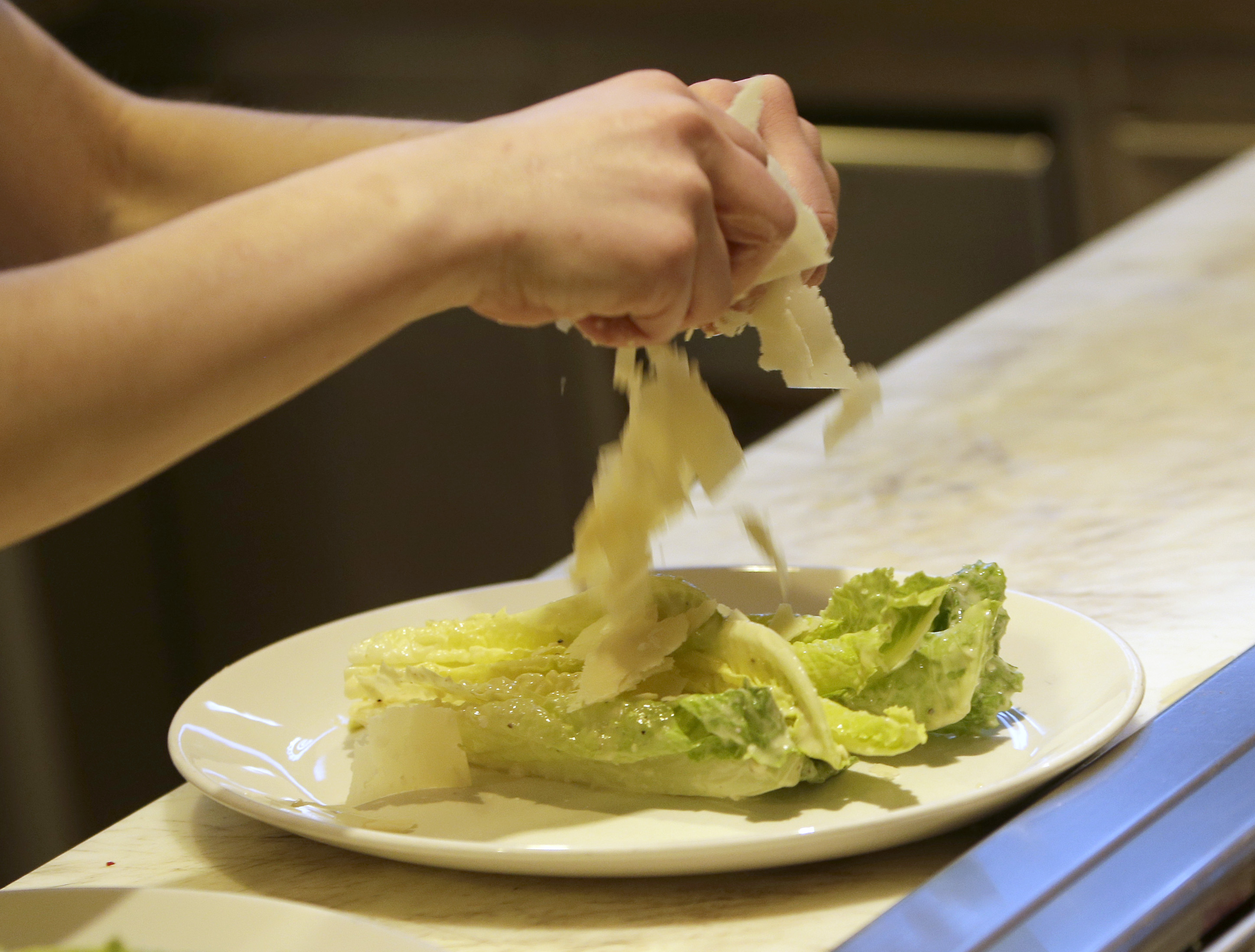 In this photo taken Tuesday,March 11, 2014,  pantry  cook Alicia Palenyy uses her bare-hands to put cheese on a salad at the Hock Farm restaurant in Sacramento, Calif. Under a bill signed last year by Gov. Jerry Brown, chefs and bartenders in California must keep bare hands off food going straight to the plate or the drink glass, and must use gloves or kitchen utensils such as tongs. (AP Photo/Rich Pedroncelli) (AP)