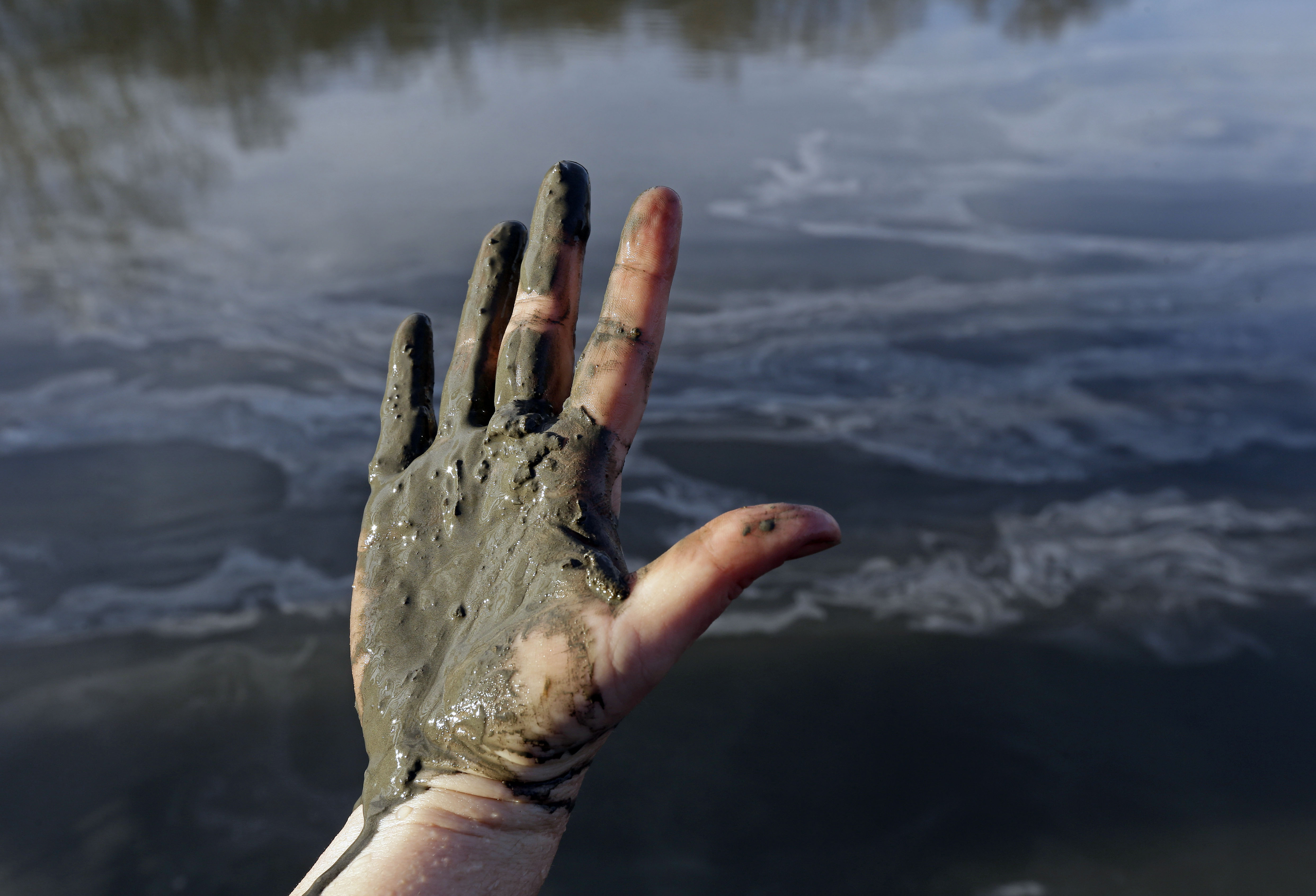 FILE - In this Feb. 5, 2014 file photo, Amy Adams, North Carolina campaign coordinator with Appalachian Voices, shows her hand covered with wet coal ash from the Dan River swirling in the background as state and federal environmental officials continued their investigations of a spill of coal ash into the river in Danville, Va. (AP/Gerry Broome)