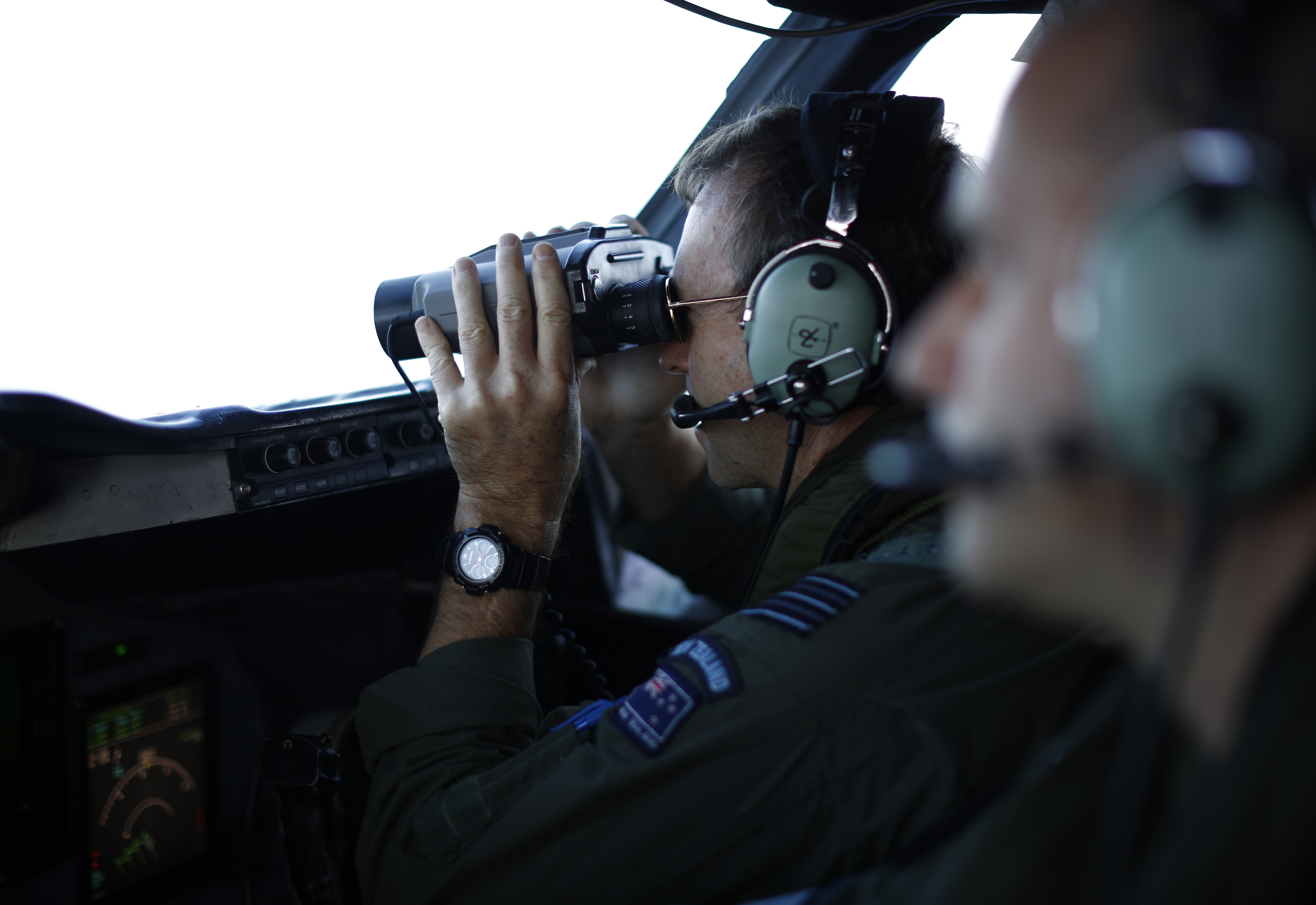 Wing Commander Rob Shearer looks through binoculars on the flight deck of a Royal New Zealand Air Force P-3K2 Orion aircraft searching for missing Malaysian Airlines flight 370 over the southern Indian Ocean, March 29, 2014.  (AP Photo/Jason Reed, Pool)