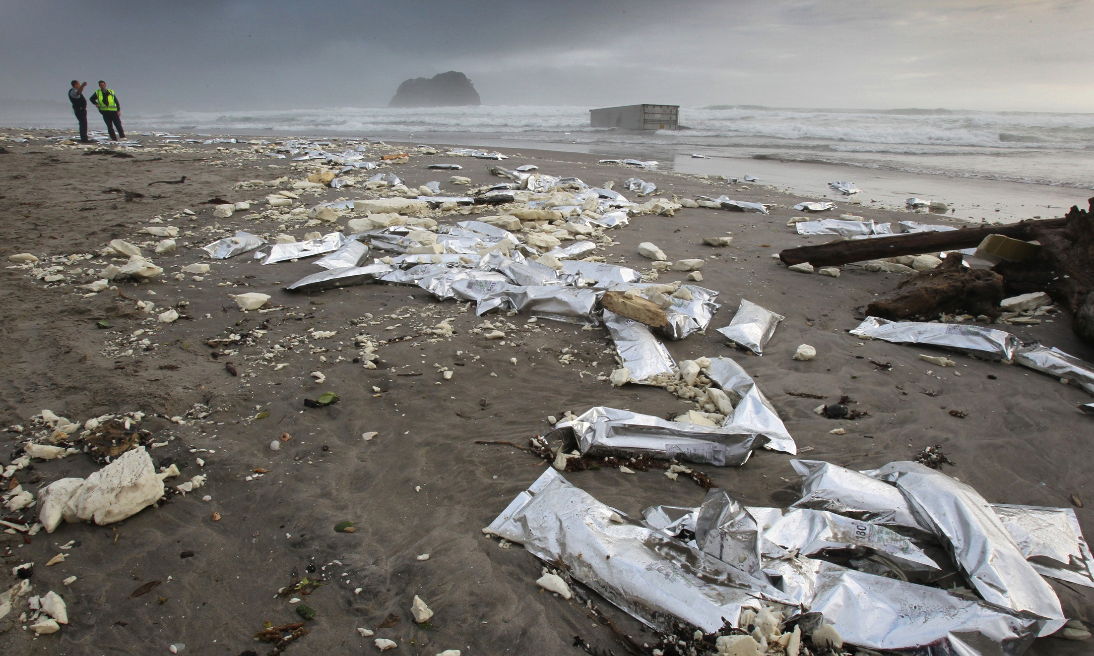 FILE - In this Oct. 13, 2011 file photo, police officers monitor debris washed ashore on the Mount Maunganui Beach as a shipping container fallen from the grounded container ship Rena sits in the breakwater near Tauranga, New Zealand.  Not only is the trash a time-wasting distraction for air and sea crews searching for debris from the Malaysia Airlines flight that vanished March 8, it also points to wider problems in the worlds oceans.  The ocean is like a plastic soup, bulked up with the croutons of these larger items, said Los Angeles captain Charles Moore, an environmental advocate credited with bringing attention to an ocean gyre between Hawaii and California known as the Great Pacific Garbage Patch. (AP Photo/New Zealand Herald, Mark Mitchell) AUSTRALIA OUT, NEW ZEALAND OUT (AP)