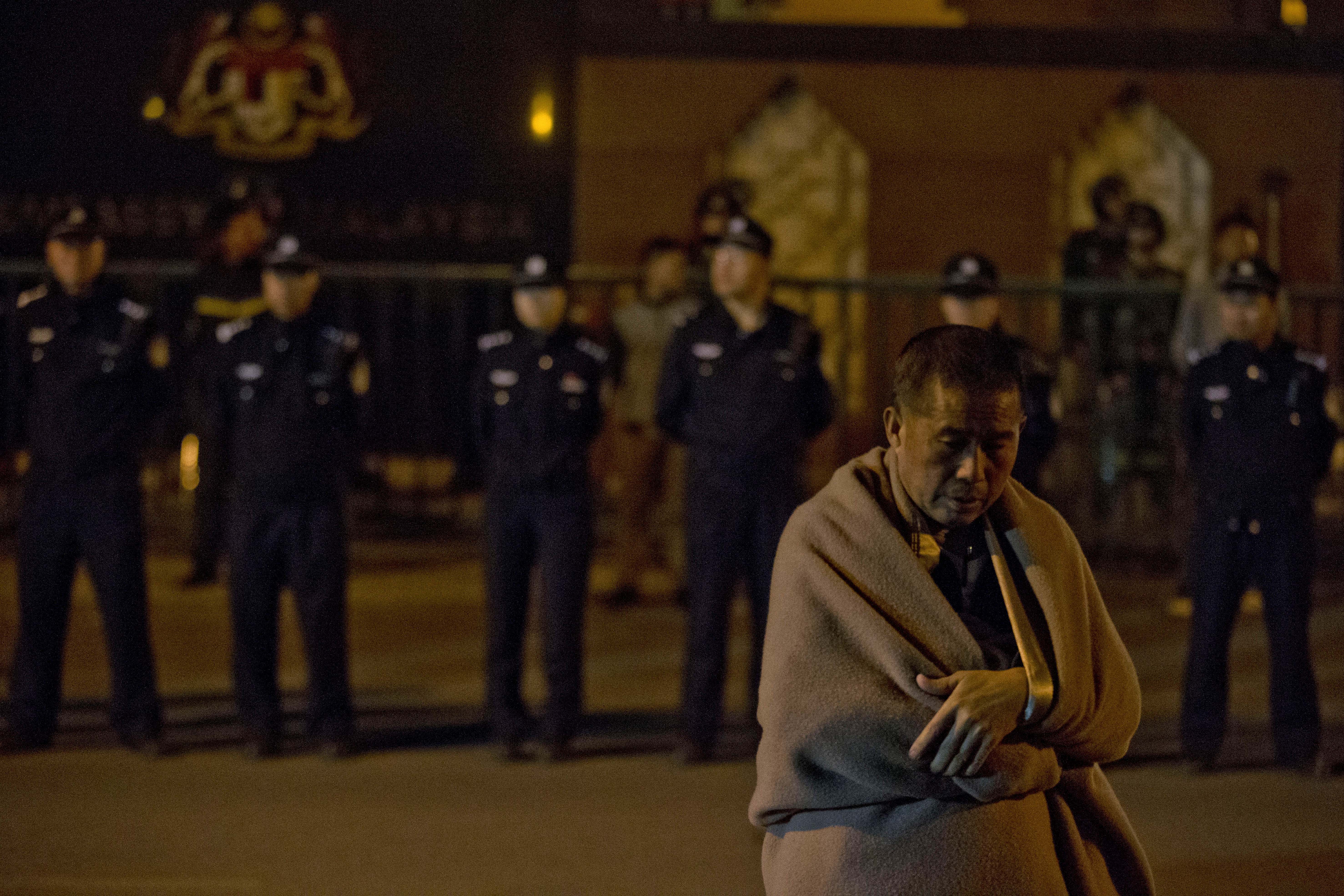 A relative of Chinese passengers onboard the Malaysia Airlines MH370 wrapped in a blanket against the cold, waits for Malaysia embassy staff to meet their demands outside the Malaysia embassy in Beijing, China, Friday, April 25, 2014. Angry relatives who had been waiting for more than 8 hours in vain for a Malaysia embassy representative to attend their daily meeting marched to the Malaysia embassy and protested through the night. (AP Photo/Ng Han Guan) (AP)
