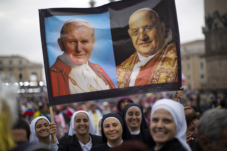 Nuns hold up a poster with portraits of  Pope John Paul II, left, and John XXIII, in St. Peter's Square at the Vatican, April 27, 2014. (AP/Emilio Morenatti)