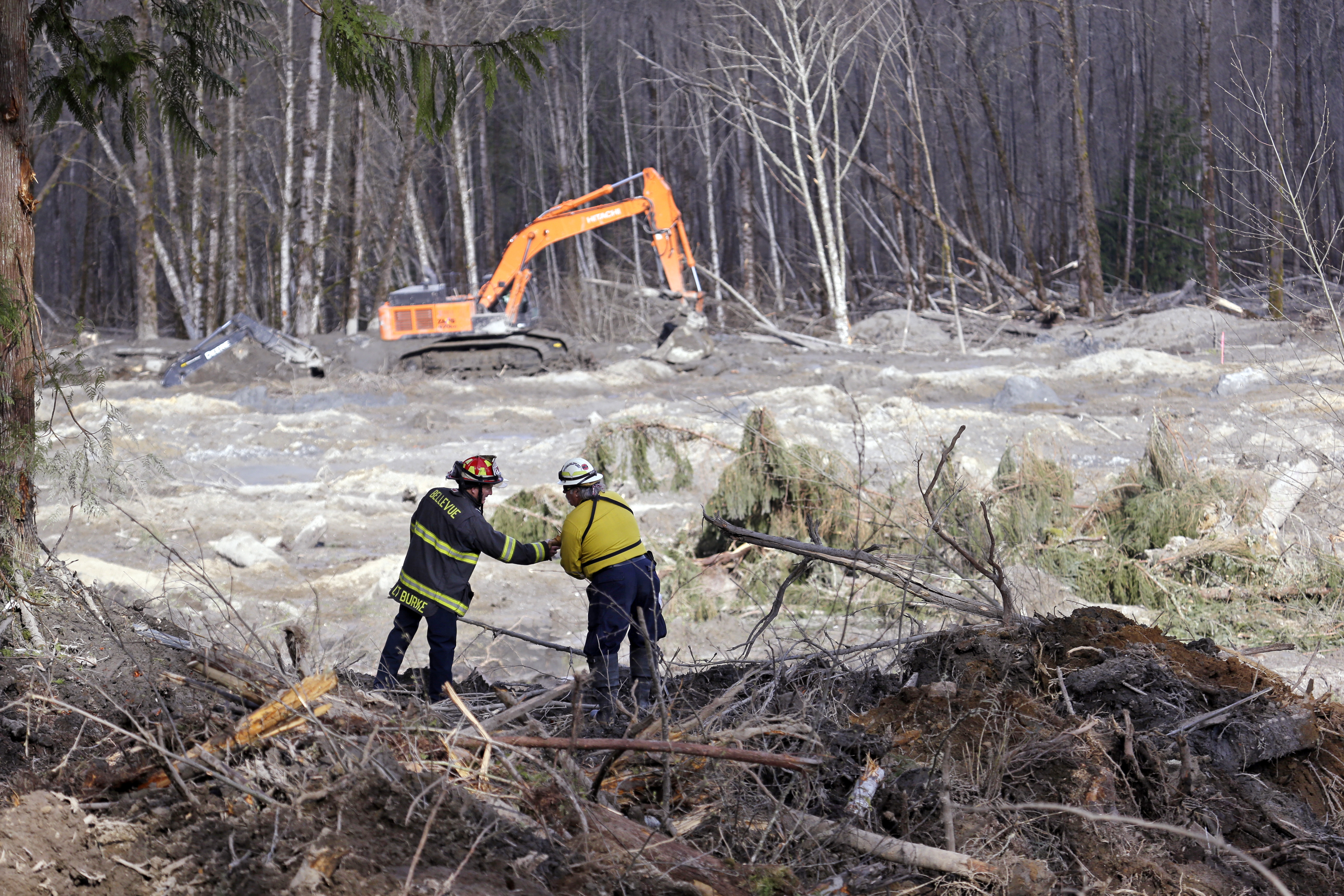 Bellevue, Wash., Fire Dept. Lt. Richard Burke, left, reaches across to shake hands with Benton County assistant fire chief Jack Coats as the two overlook the scene of a deadly mudslide Wednesday, April 2, 2014, in Oso, Wash. (AP Photo/Elaine Thompson)