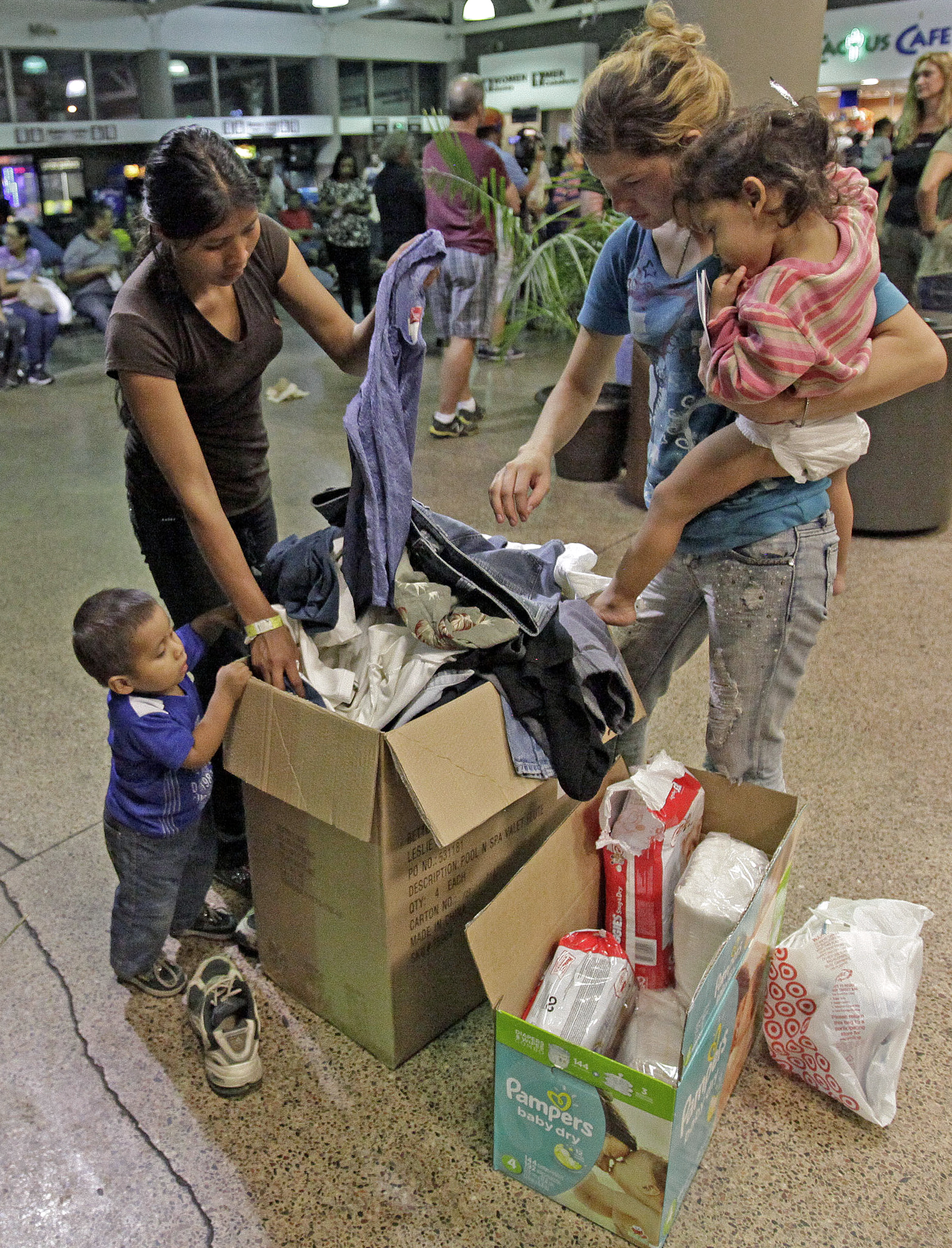 Women and children look through a box of cloths that were donated by volunteers at the Greyhound bus terminal, Thursday, May 29, 2014 in Phoenix.  About 400 mostly Central American women and children caught crossing from Mexico into south Texas were flown to Arizona this weekend after border agents there ran out of space and resources.  Officials then dropped hundreds of them off at Phoenix and Tucson Greyhound stations, overwhelming the stations and humanitarian groups who were trying to help. (AP Photo/Rick Scuteri) (AP)